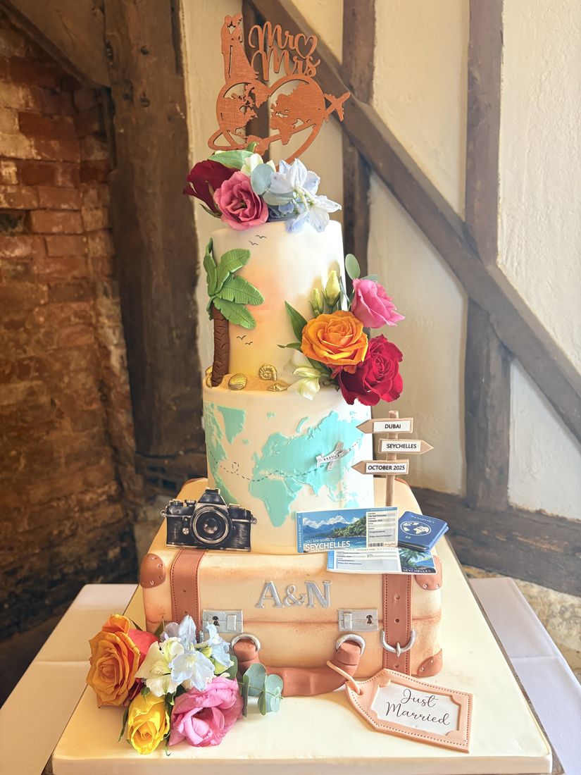 Travel-themed wedding cake with a world map, vintage suitcase and sugar roses