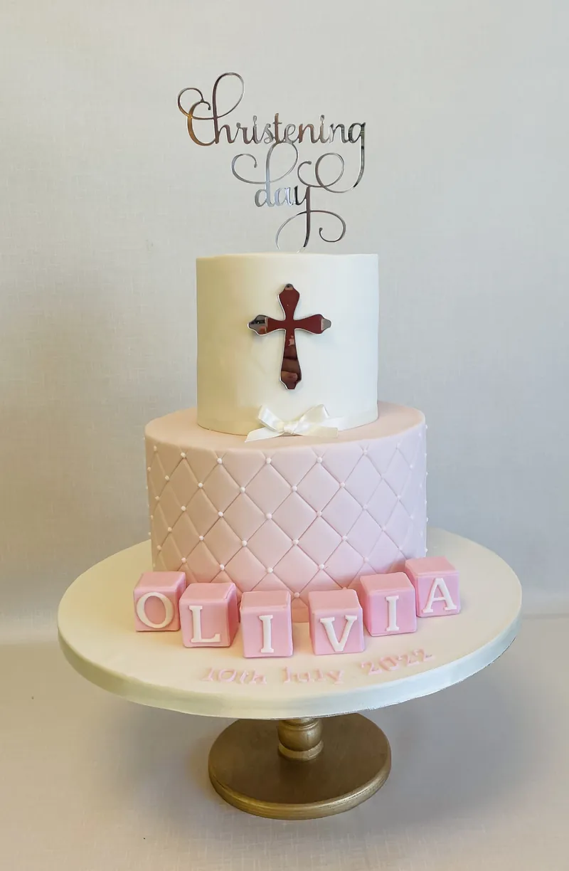 Two-tier christening cake with a cross, pink quilting and Olivia name blocks by Catherine Scott