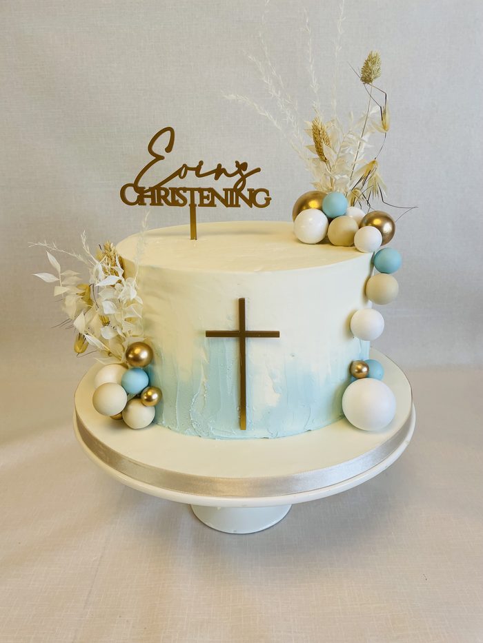 Boho style christening cake with dried grasses, sugar balls and a gold cross topper
