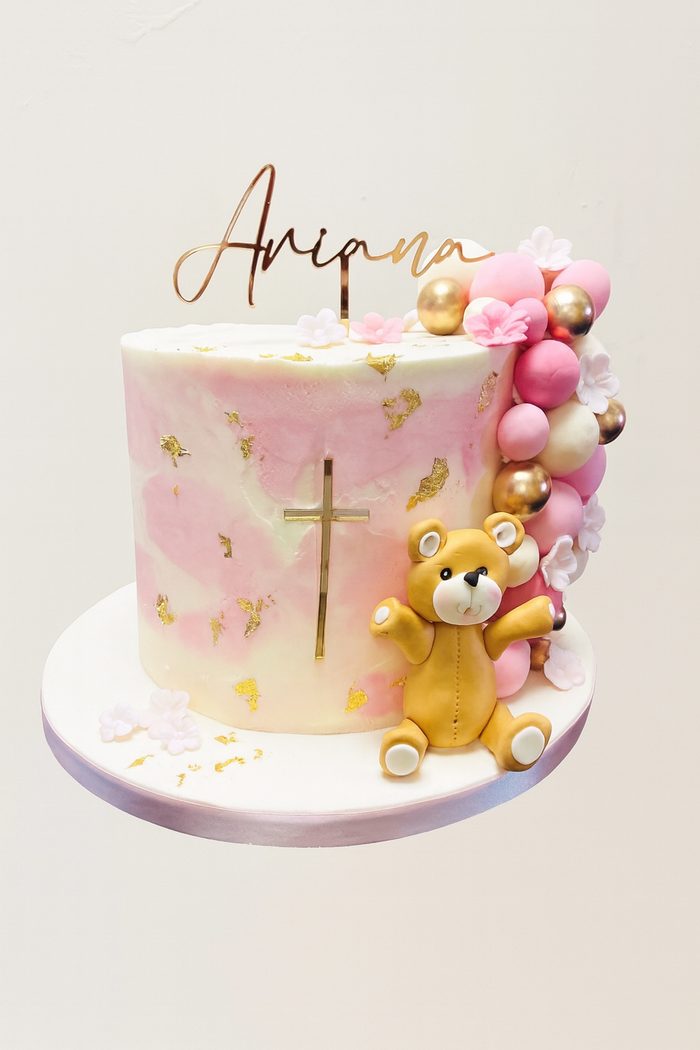 Marble effect buttercream christening cake in pink and gold with a handmade teddy, sugar balls and a personalised name topper