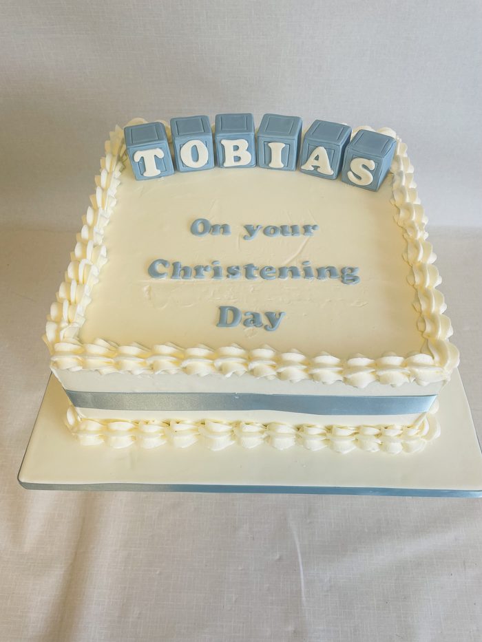 Square buttercream christening cake with a piped border and name blocks spelling Tobias
