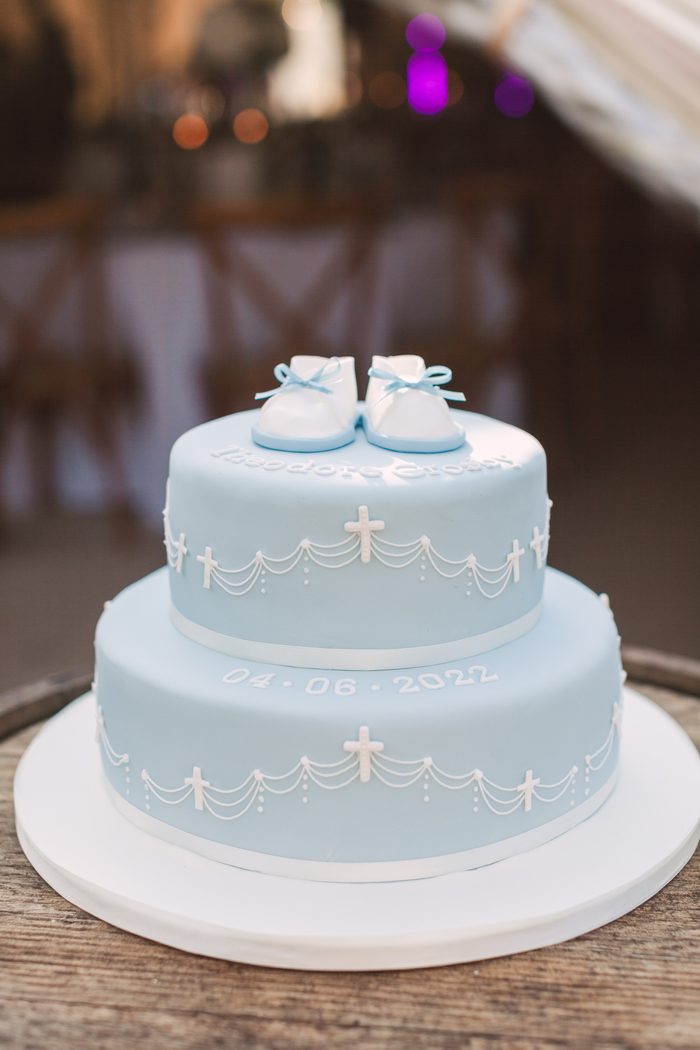 Two tier pale blue christening cake with piped crosses and sugar bootees on the top tier