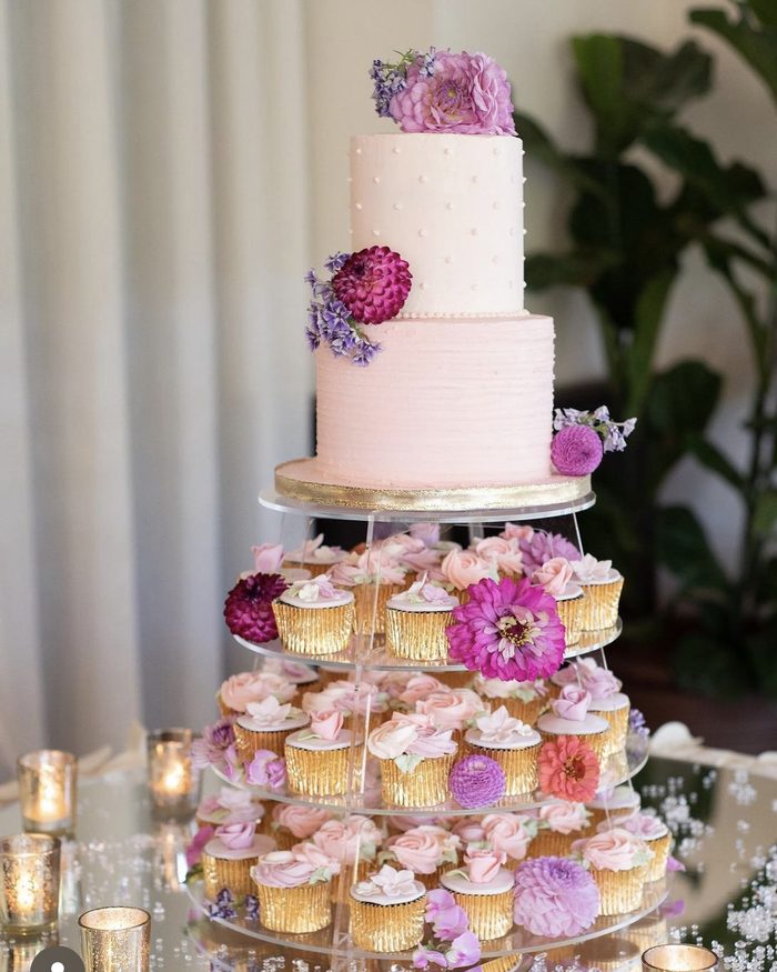 Two-tier blush wedding cake on a cupcake tower with pink and purple flowers by Catherine Scott